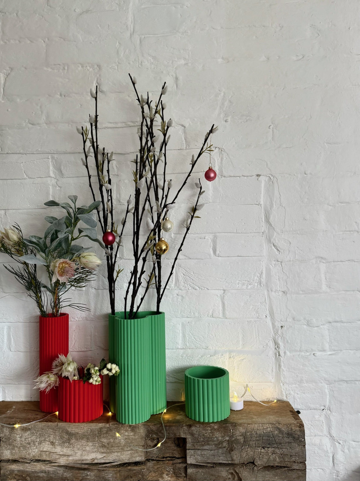 Set of red and green Curve Vases in small, medium and large on a wooden mantel