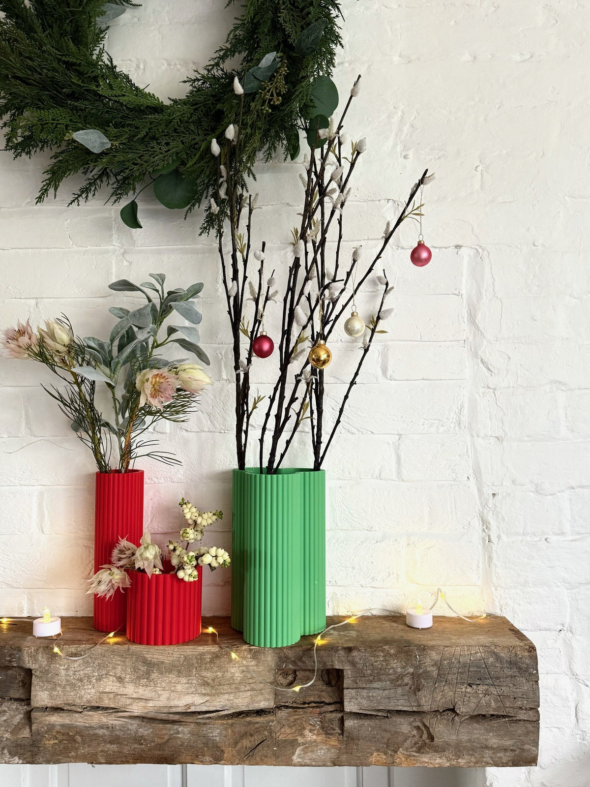 Red and green fluted Curve Vases on a festive mantelpiece with Christmas branches and baubles