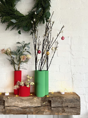 Red and green fluted Curve Vases on a festive mantelpiece with Christmas branches and baubles