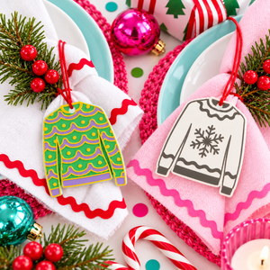 Christmas jumper decorations tied to napkins on a festive pink and white table